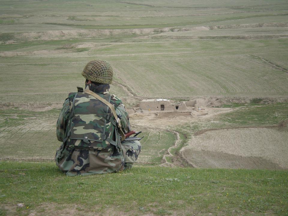 Soldier sits on a hill overlooking an outpost building
