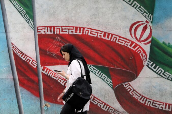 A woman wearing a hijab walks past a mural depicting the flag of Iran in Tehran, April 2023. Photo by Fatemeh Bahrami/Anadolu Agency via Getty Images