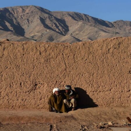 Two Afghan men talk as they sit beside a mud wall in the outskirts of Herat, Afghanistan (December 2014). Photo by Aref Karimi / AFP via Getty Images