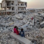 Children are seen sitting amongst the rubble of buildings destroyed by the earthquake in the city of Jenderes in Aleppo, northwestern Syria (February 2023)
