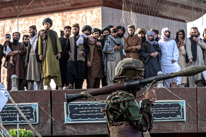 Men watch as an armed Taliban security personnel rides a vehicle convoy during a parade in Kabul.