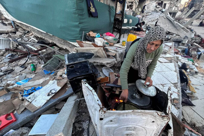 A woman cooks breakfast in the rubble of her house