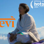 Devi film poster showing a woman sitting cross-legged against a blue sky