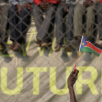 A hand waves a South Sudan flag in front of the word 'future'