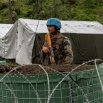 An Indian peacekeeper stands behind a fence in front of a tent