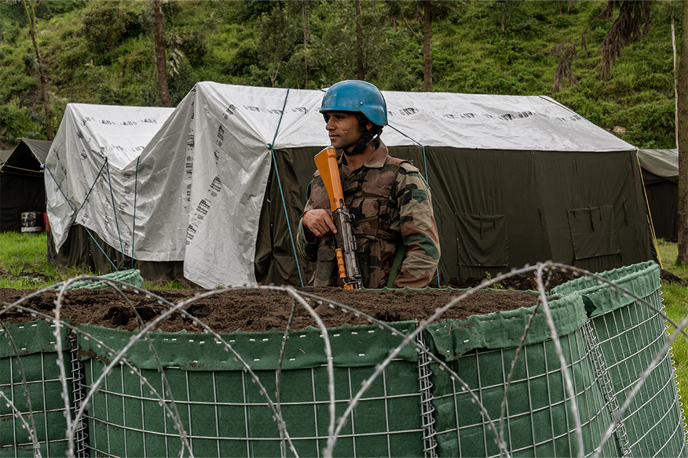 An Indian peacekeeper stands behind a fence in front of a tent