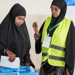 A woman casts her vote as an official looks on